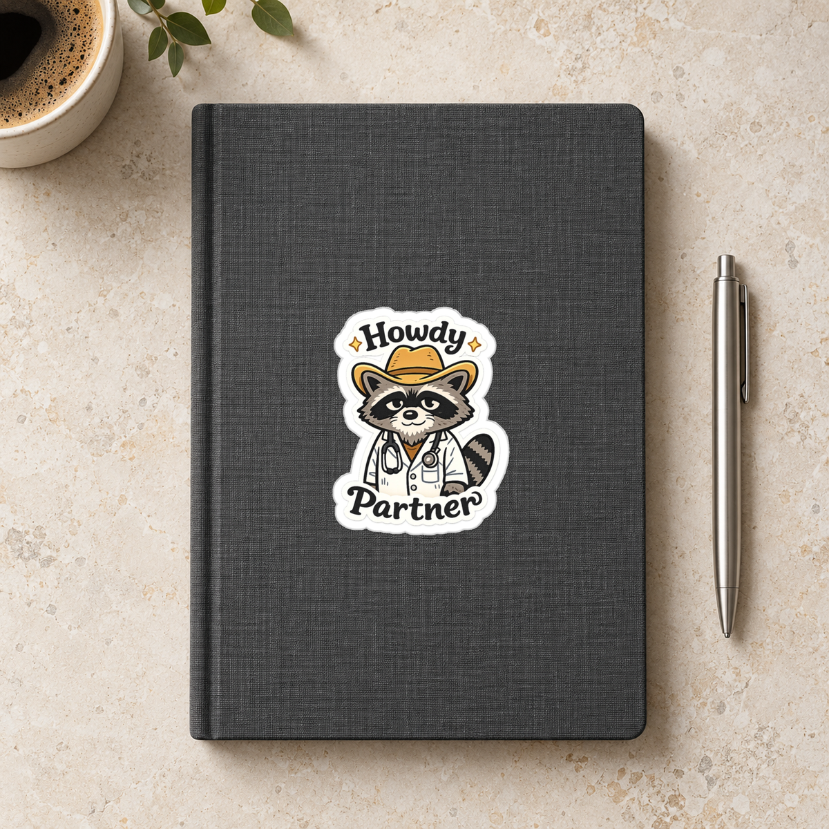 Howdy Partner Raccoon Doctor Sticker in the 3 × 3 inch size shown on a charcoal notebook in an illustrative lifestyle mockup