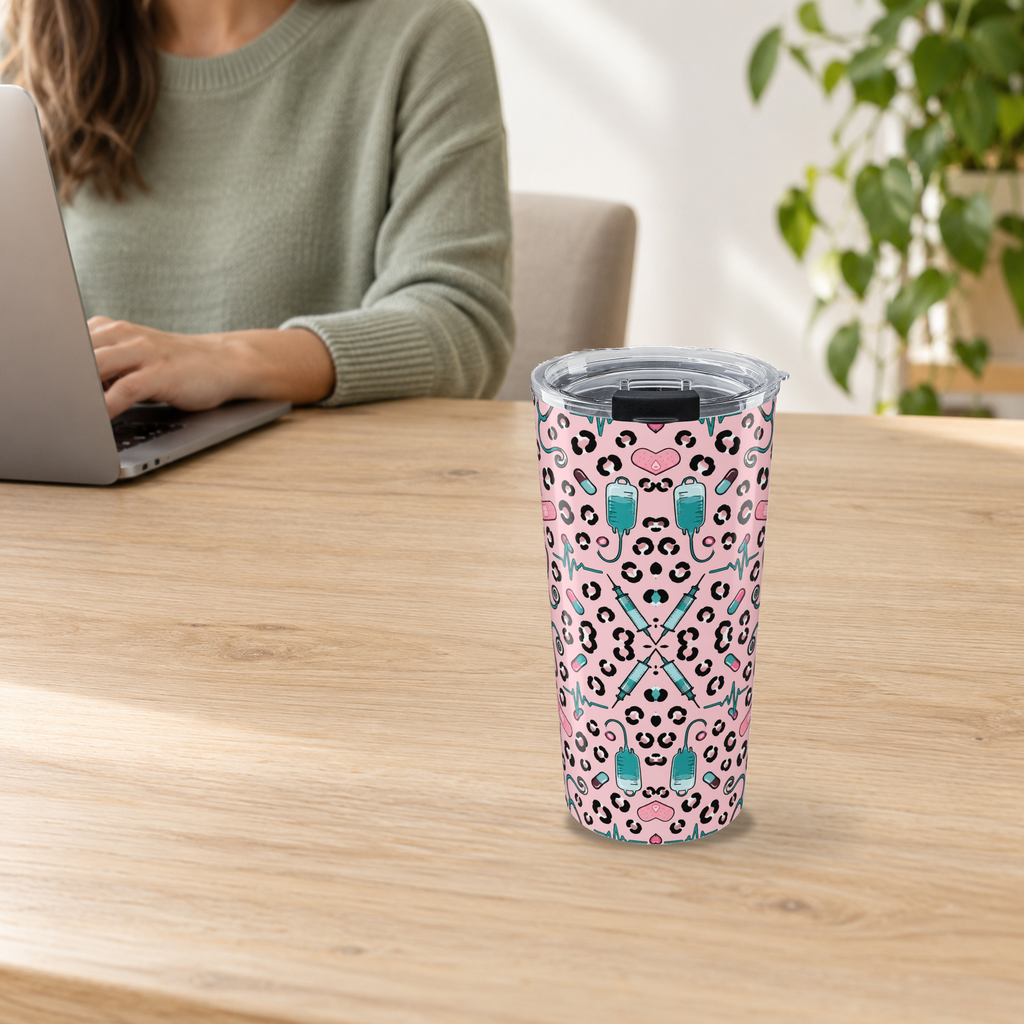 Pink Leopard Stethoscope Tumbler in the 20oz size on a wooden desk beside an adult using a laptop