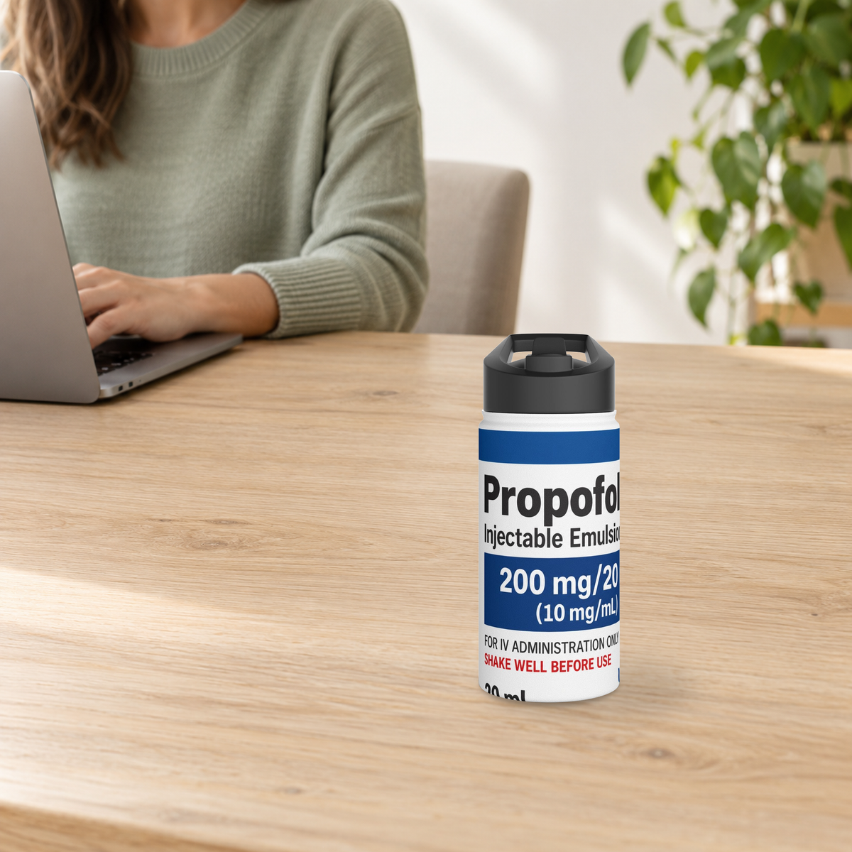Novelty 12oz white water bottle with Propofol-inspired print on a wooden desk beside an adult using a laptop