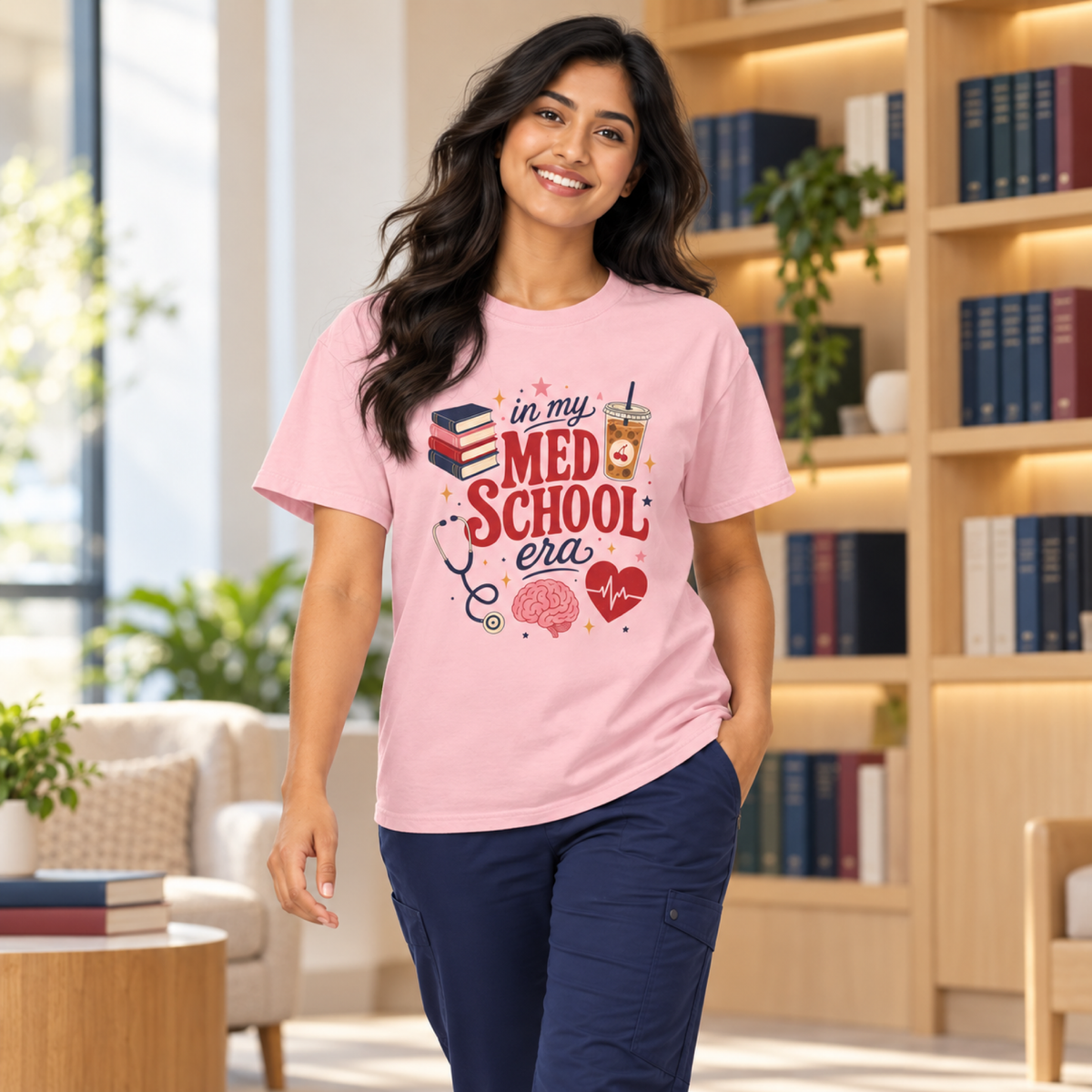 Medical student wearing a Blossom pink In My Med School Era tee and navy scrub trousers in a warm study lounge