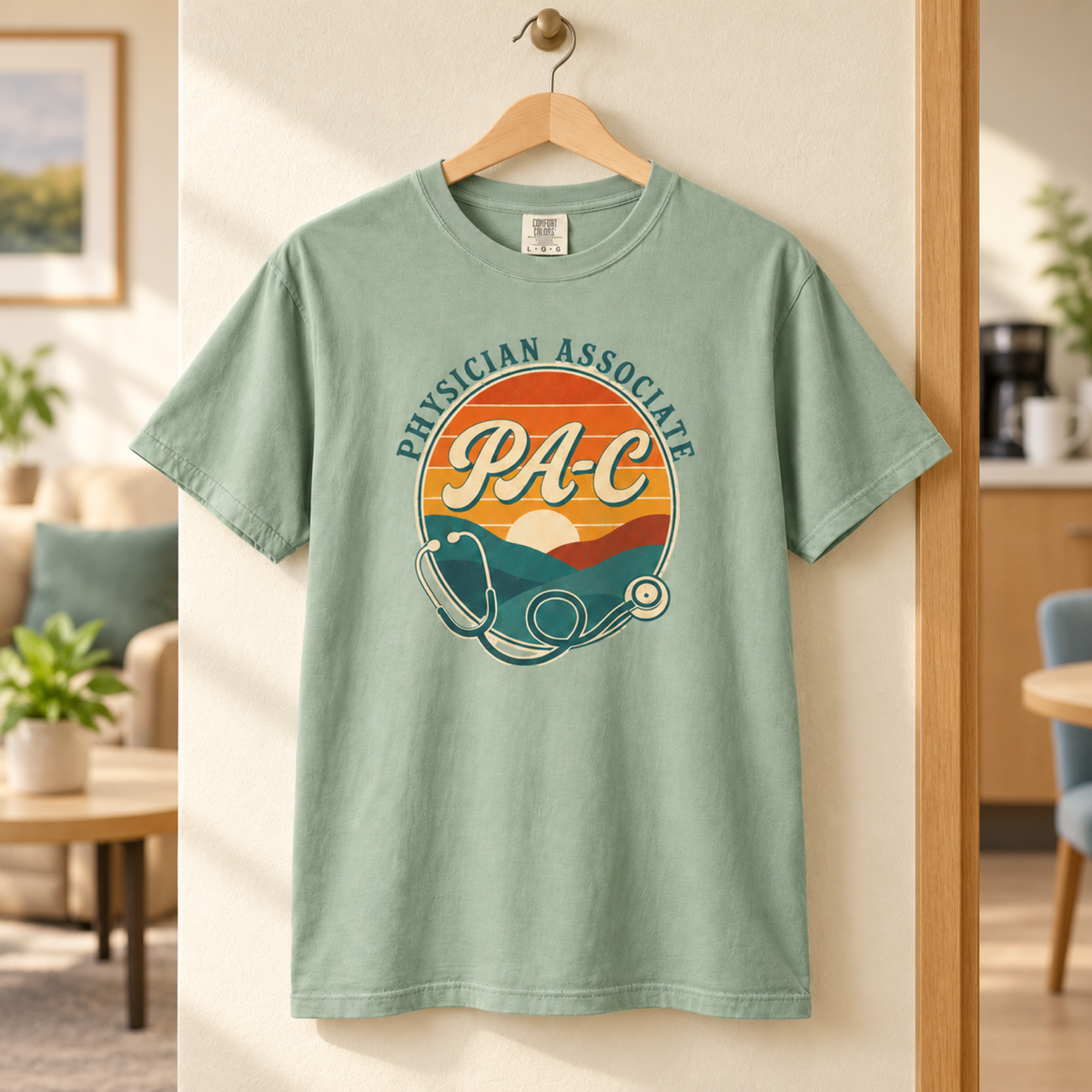 Bay green Physician Associate PA-C sunset tee on a wooden hanger in a tidy medical staff lounge