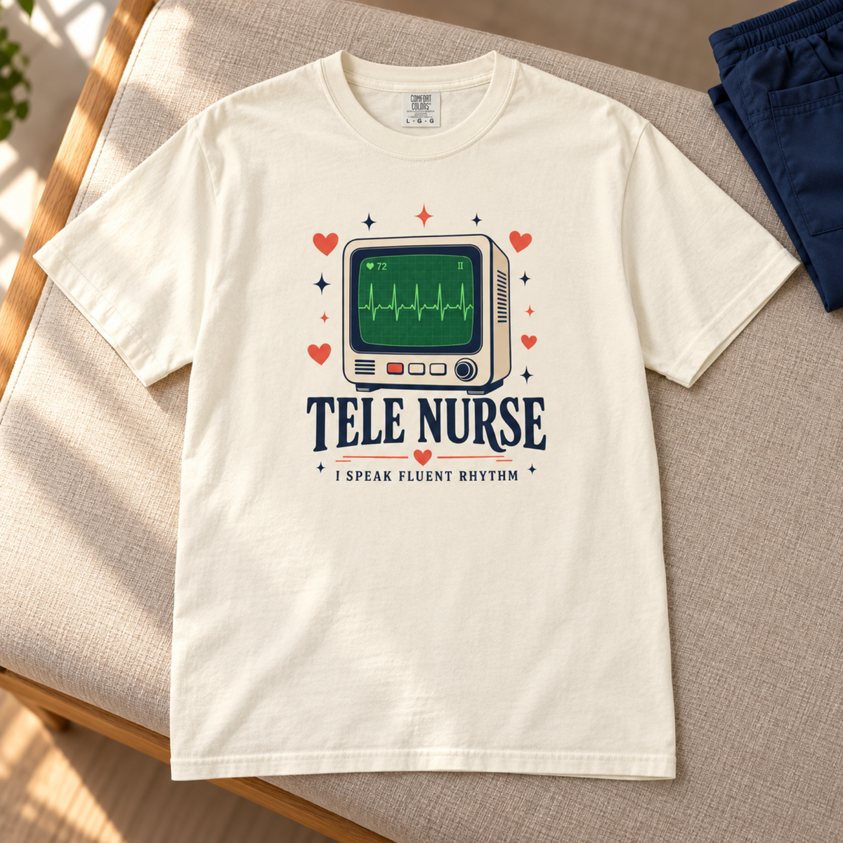 Ivory Tele Nurse Fluent Rhythm tee flat lay on a warm linen bench in a medical staff lounge
