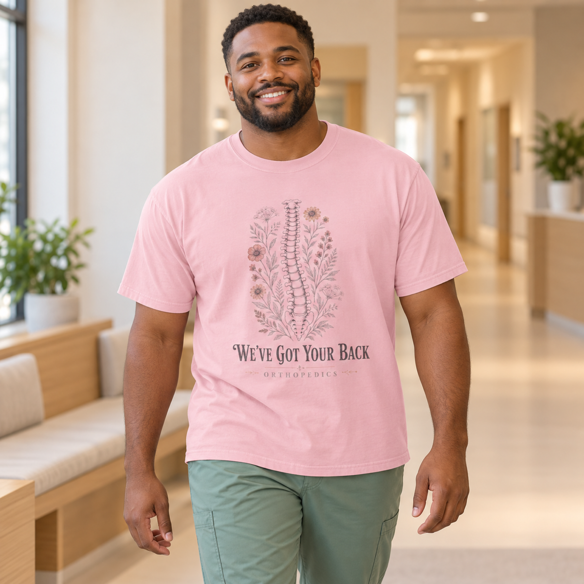 Healthcare professional wearing a Blossom pink Orthopedics floral spine tee and sage scrub trousers in a warm clinic lounge