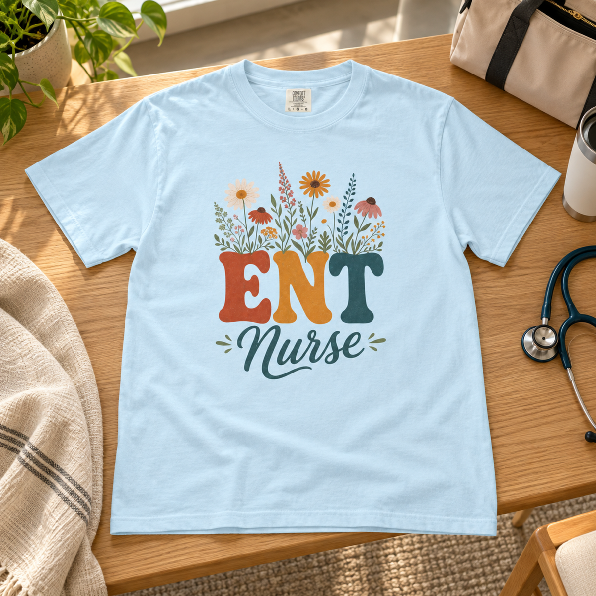Chambray blue wildflower ENT Nurse tee laid flat on a warm oak clinic staff-lounge bench