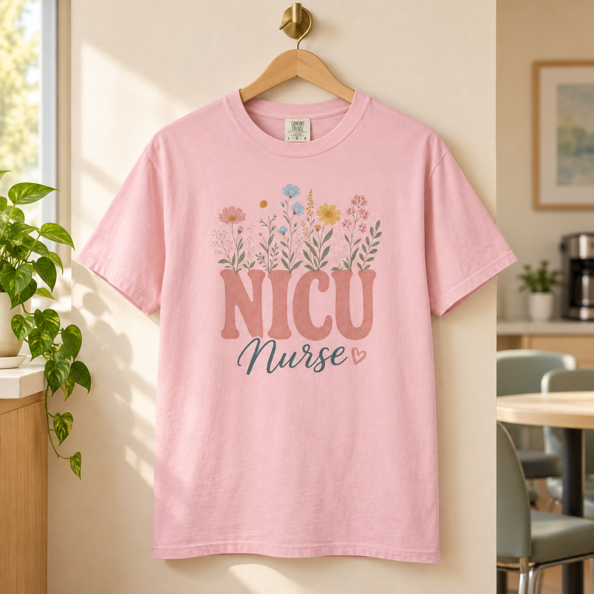 Blossom pink pastel wildflower NICU Nurse tee on a wooden hanger in a warm hospital staff lounge
