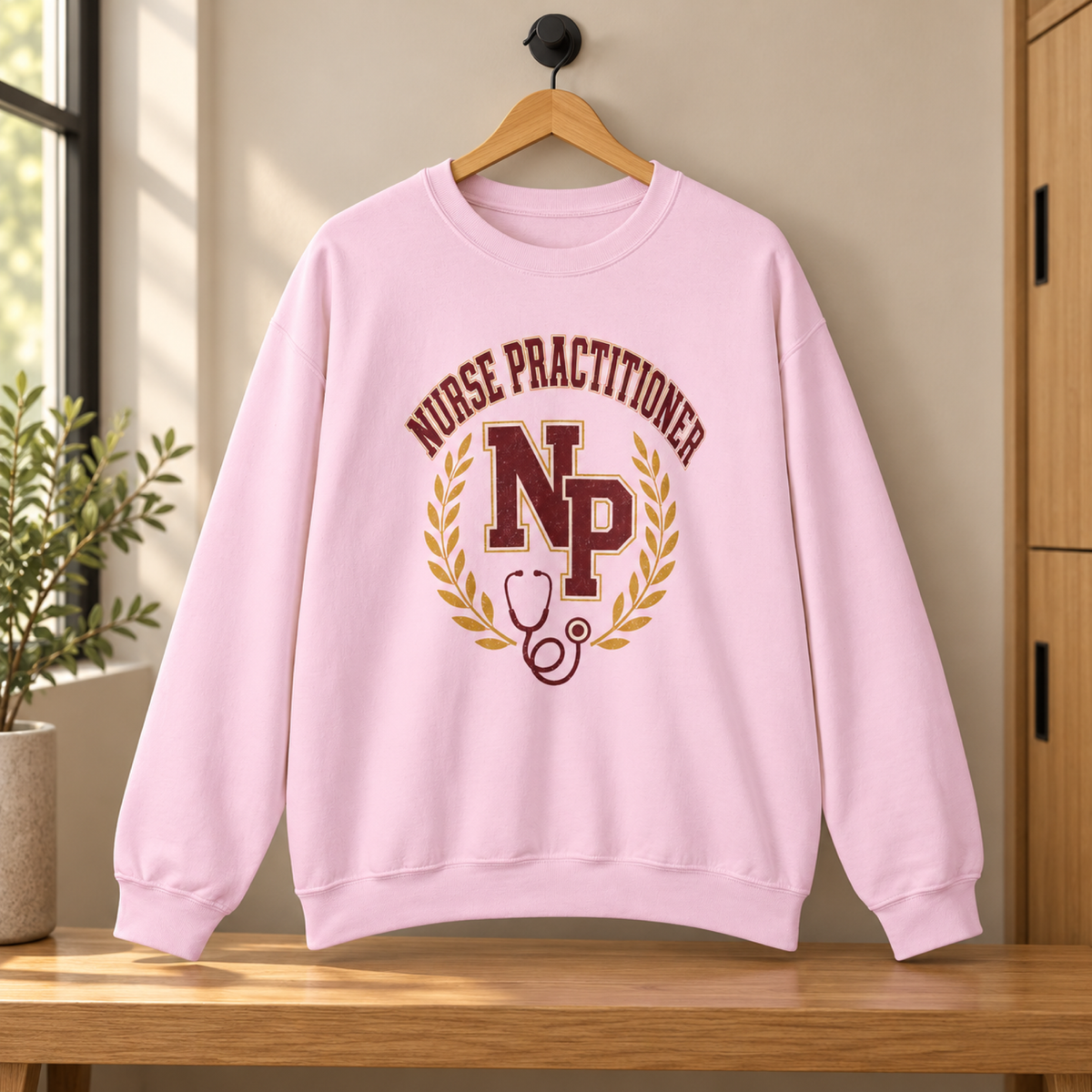Light Pink Nurse Practitioner NP Gildan 18000 sweatshirt on a hanger in a tidy staff lounge