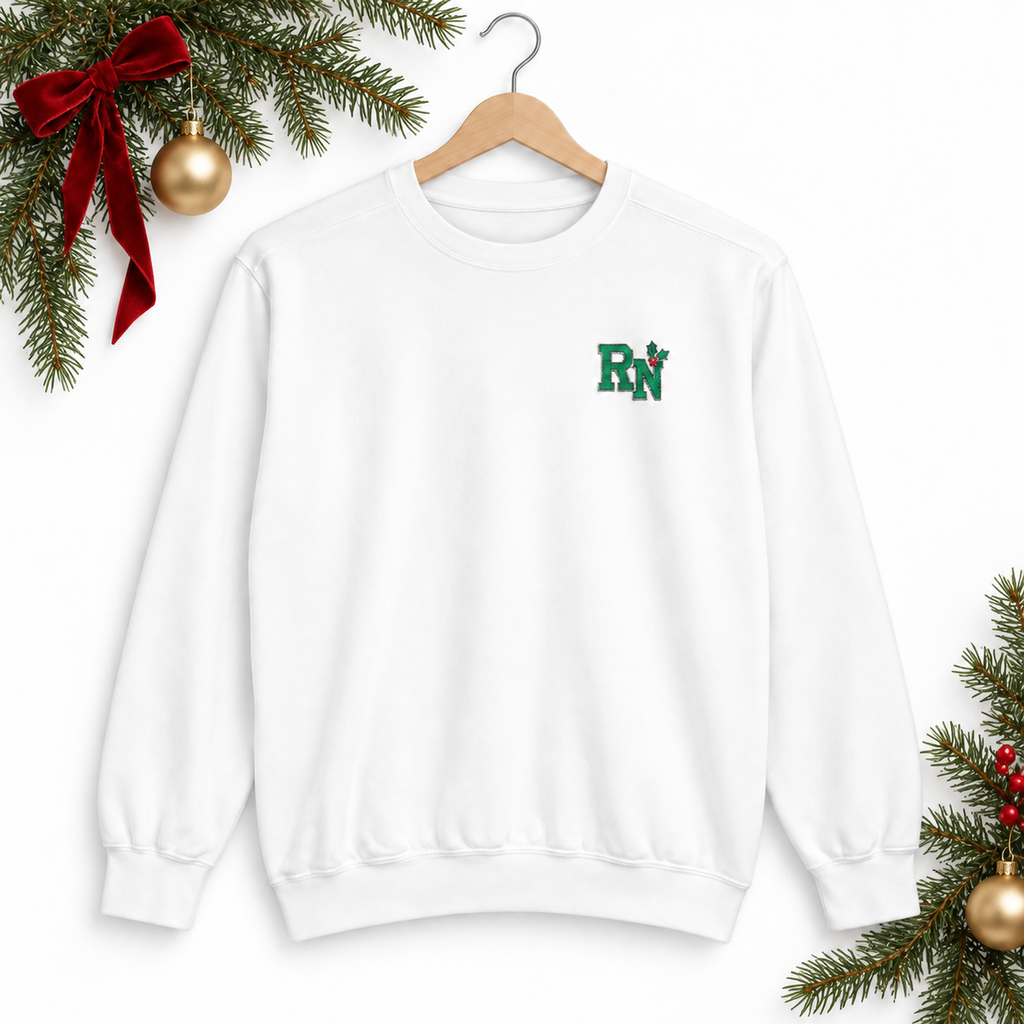 White Comfort Colors RN holly embroidered sweatshirt on a hanger with Christmas greenery and ribbon against white